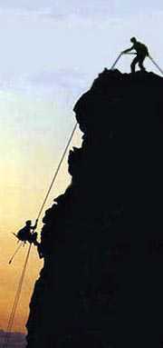 men climbing face of cliff at sunset
